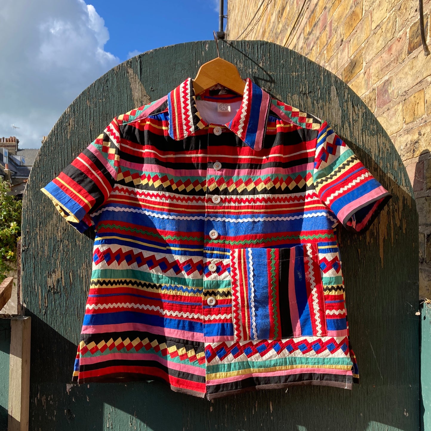 A short-sleeved shirt made from brightly coloured seminole patchwork hanging on a wooden gate