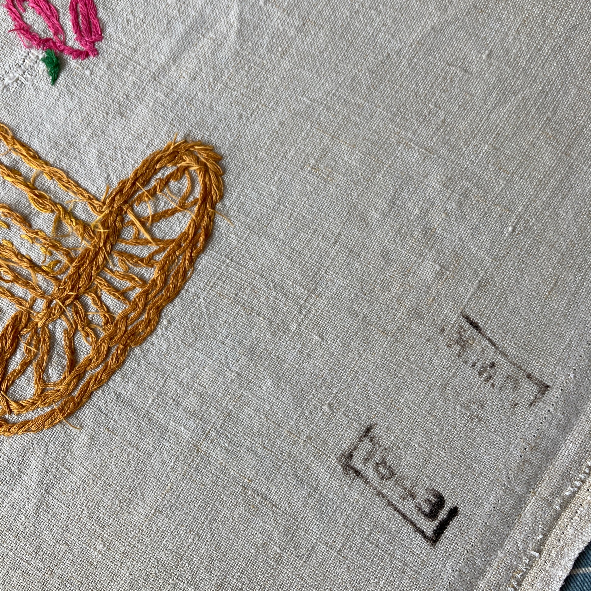 Close-up of prison stamp from 1943 on a short-sleeved shirt made from recycled tablecloths is mainly white and off-white with colourful embroidered and appliquéd flowers and orange buttons