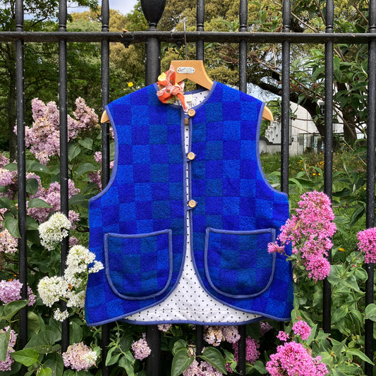 Vest/gilet/waistcoat made from a reclaimed blue checkerboard weave Irish wool Gaiety blanket, photographed in front of a lilac bush
