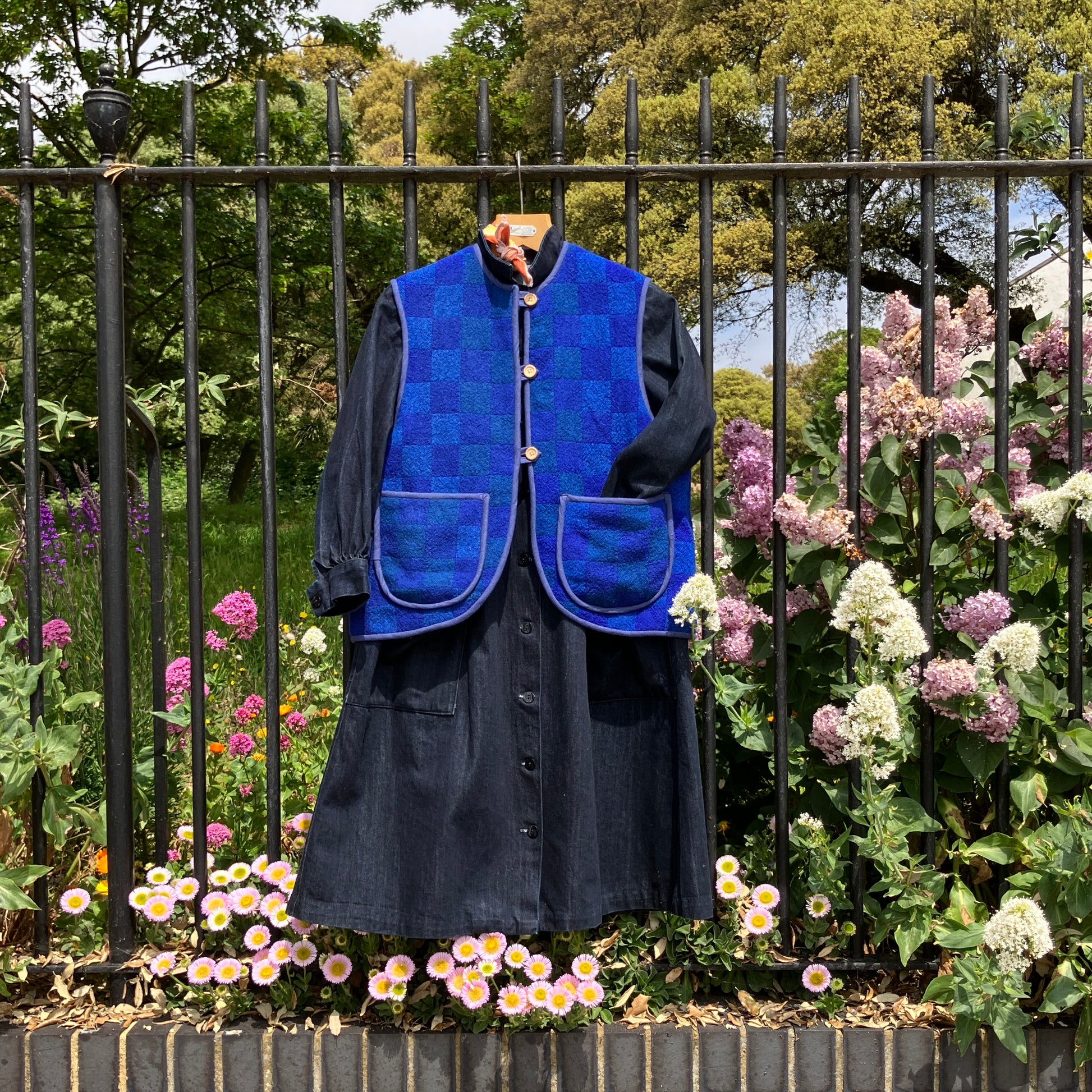 Vest/gilet/waistcoat made from a reclaimed blue checkerboard weave Irish wool Gaiety blanket, photographed with a denim midi dress underneath and in front of a lilac bush