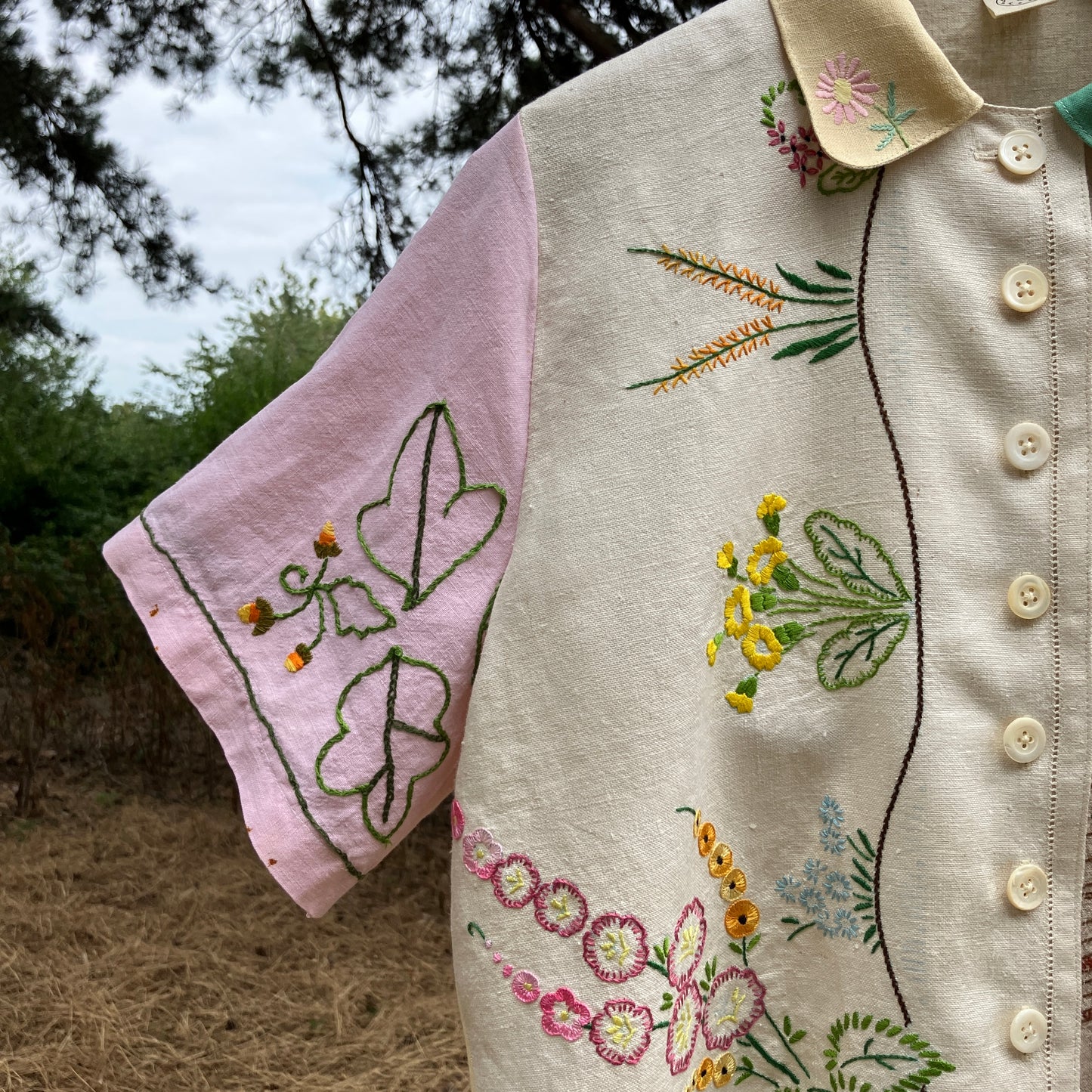 A short-sleeve button-front shirt made from reclaimed vintage tablecloths in neutrals with pink sleeves, and a light green collar.