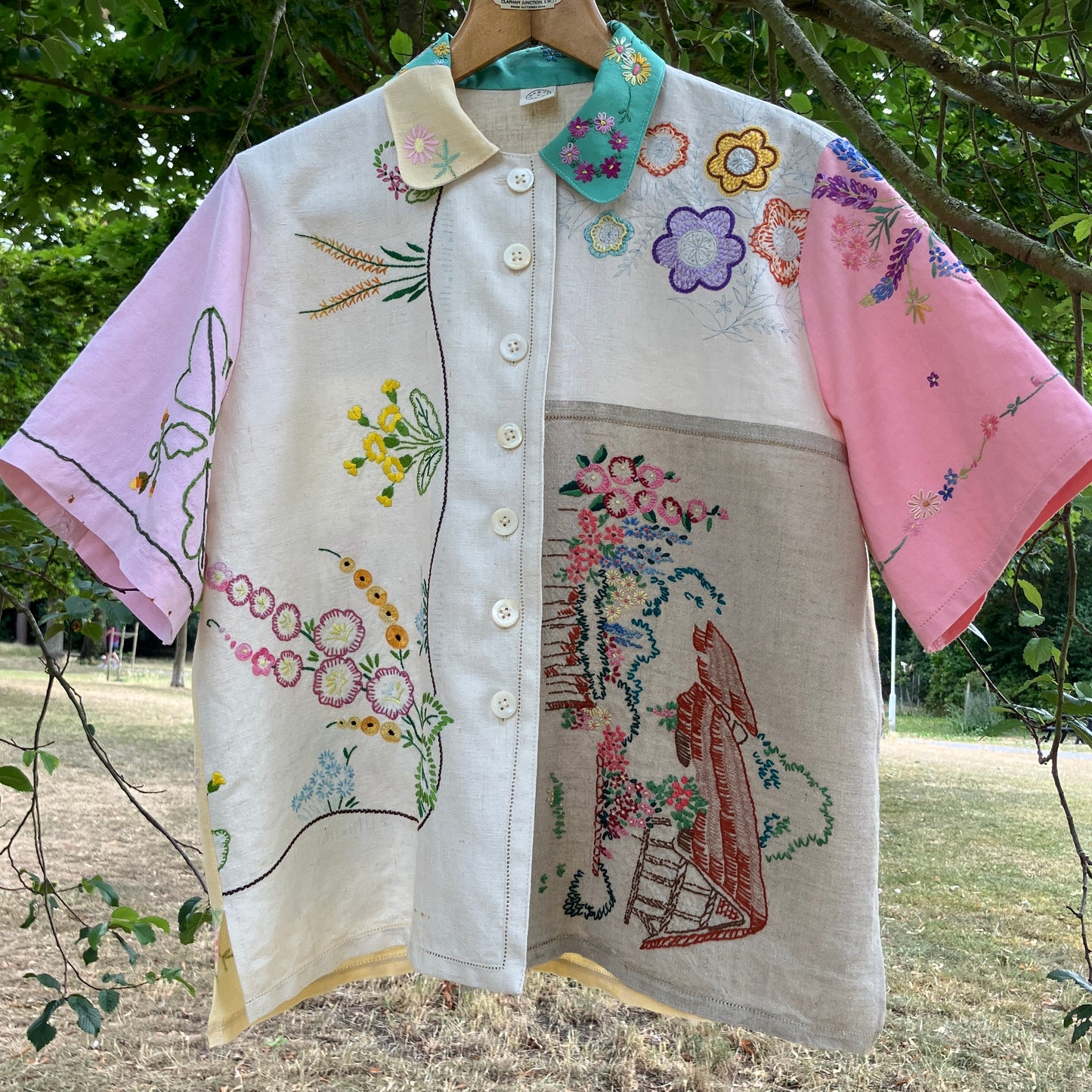 A short-sleeve button-front shirt made from reclaimed vintage tablecloths in neutrals with pink sleeves, and a light green collar.