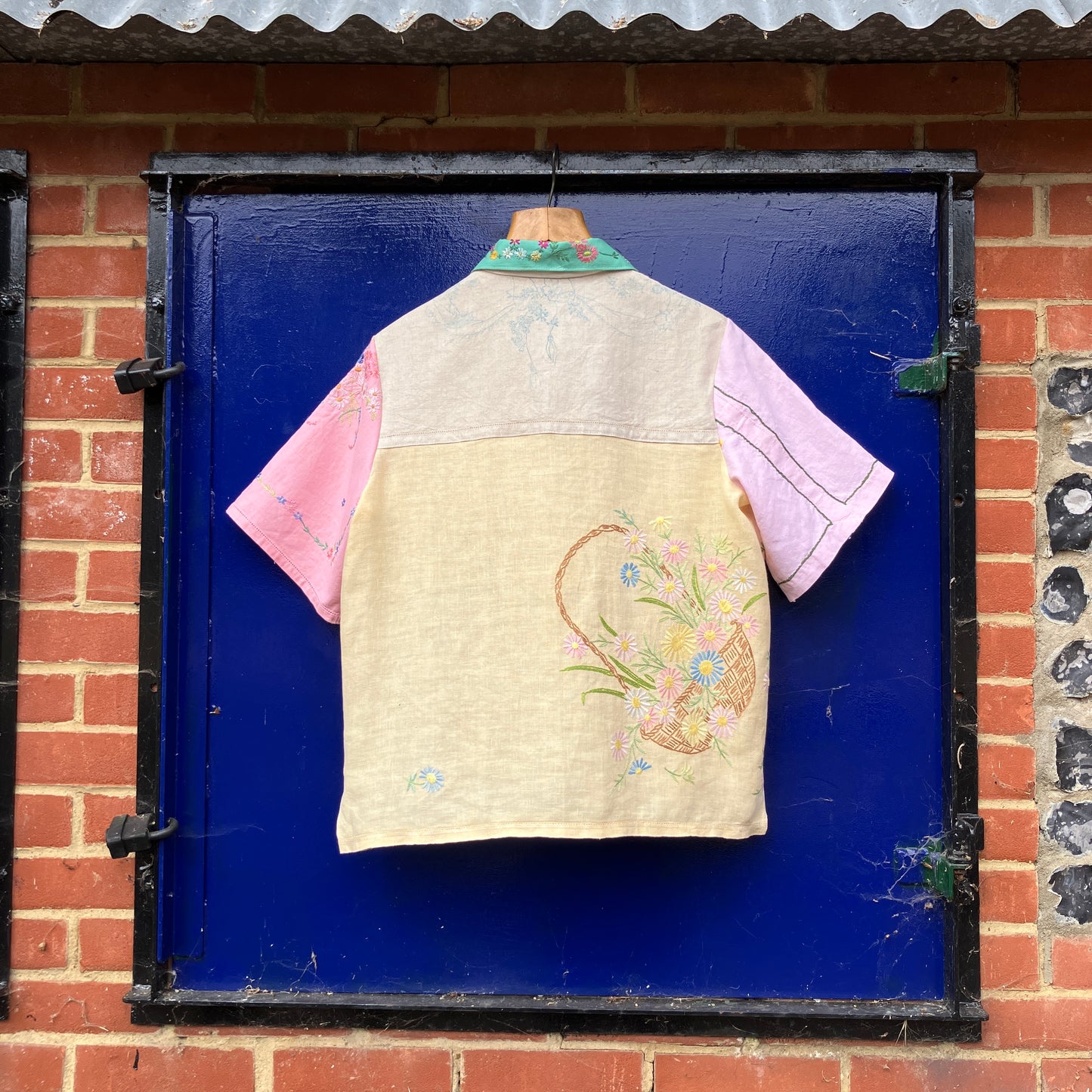 A short-sleeve button-front shirt made from reclaimed vintage tablecloths in neutrals with pink sleeves, and a light green collar.