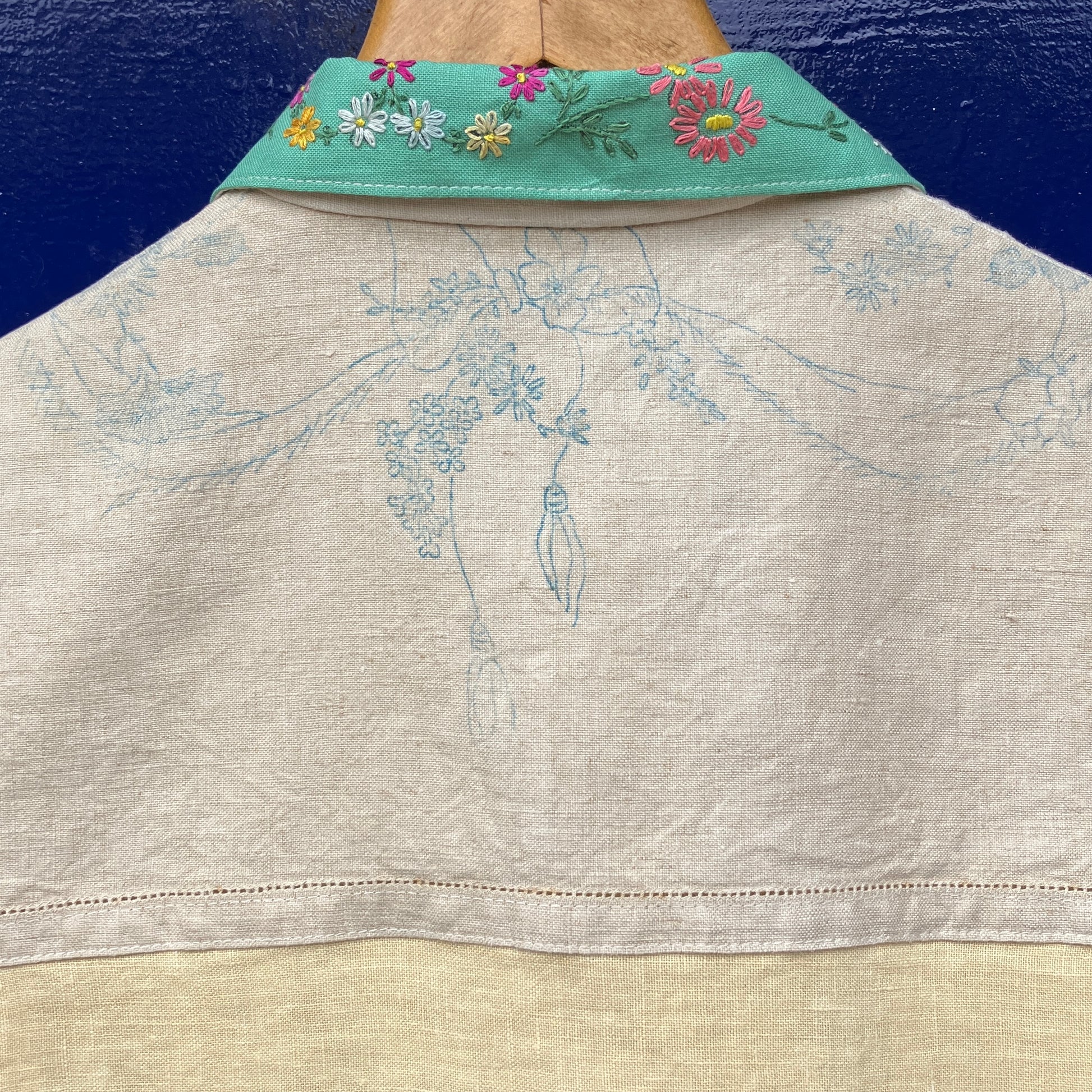 A short-sleeve button-front shirt made from reclaimed vintage tablecloths in neutrals with pink sleeves, and a light green collar.