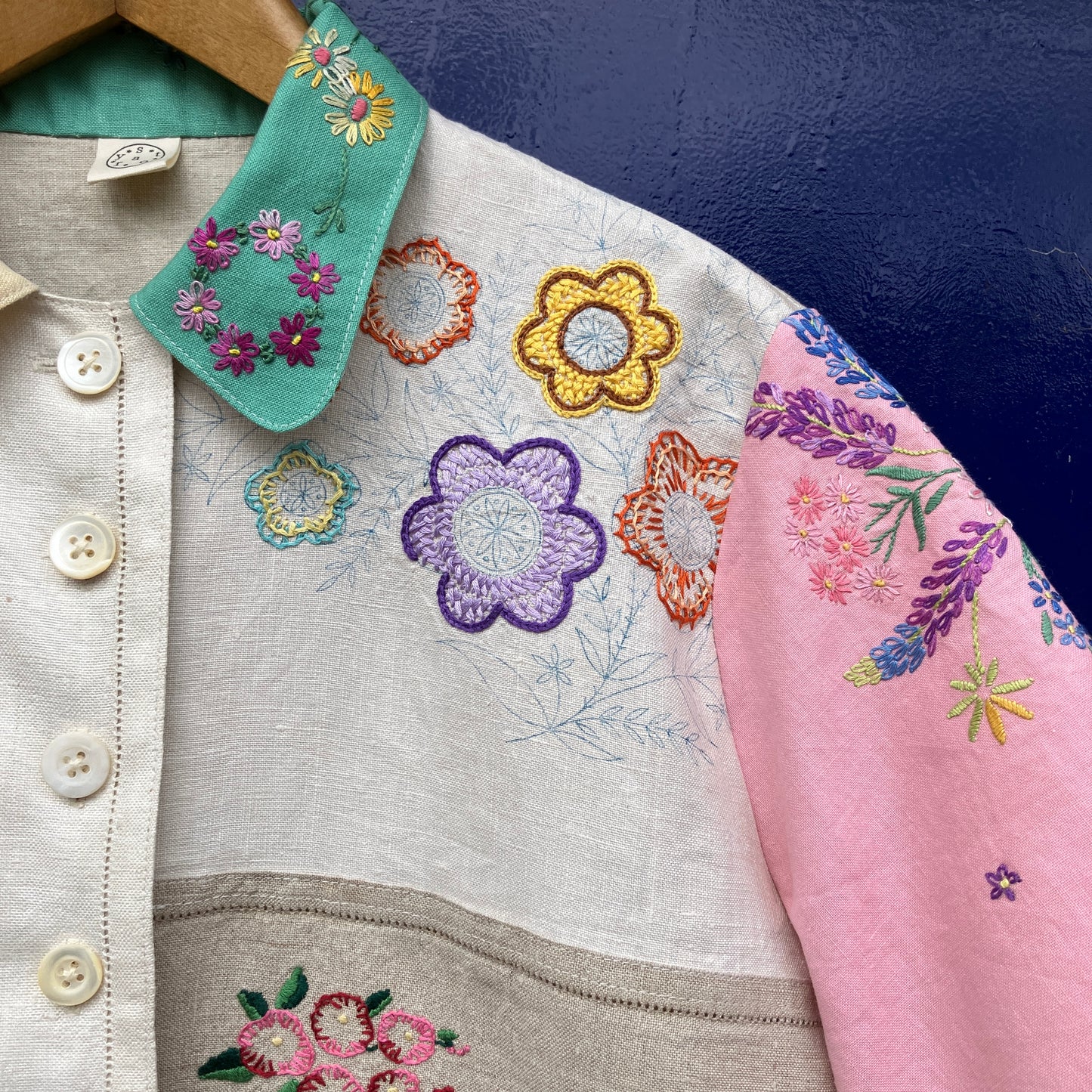 A short-sleeve button-front shirt made from reclaimed vintage tablecloths in neutrals with pink sleeves, and a light green collar.
