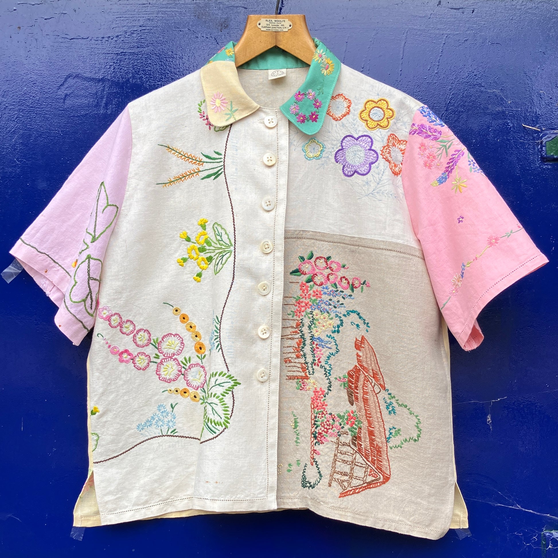 A short-sleeve button-front shirt made from reclaimed vintage tablecloths in neutrals with pink sleeves, and a light green collar.
