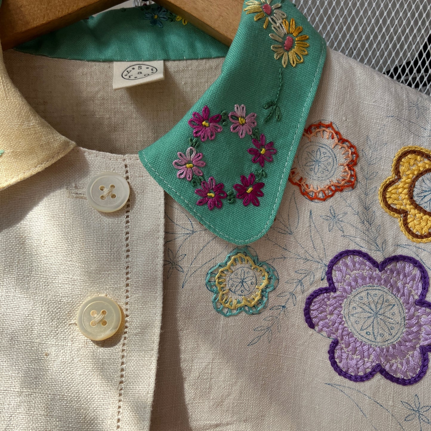 A short-sleeve button-front shirt made from reclaimed vintage tablecloths in neutrals with pink sleeves, and a light green collar.