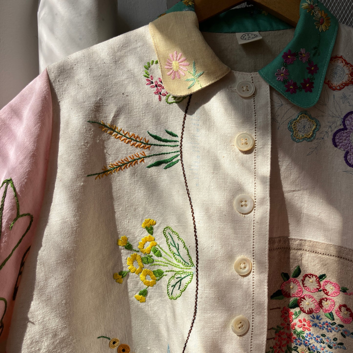 A short-sleeve button-front shirt made from reclaimed vintage tablecloths in neutrals with pink sleeves, and a light green collar.