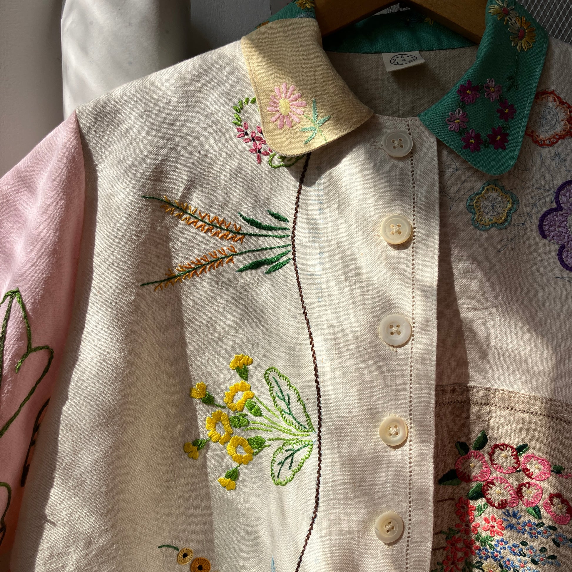 A short-sleeve button-front shirt made from reclaimed vintage tablecloths in neutrals with pink sleeves, and a light green collar.