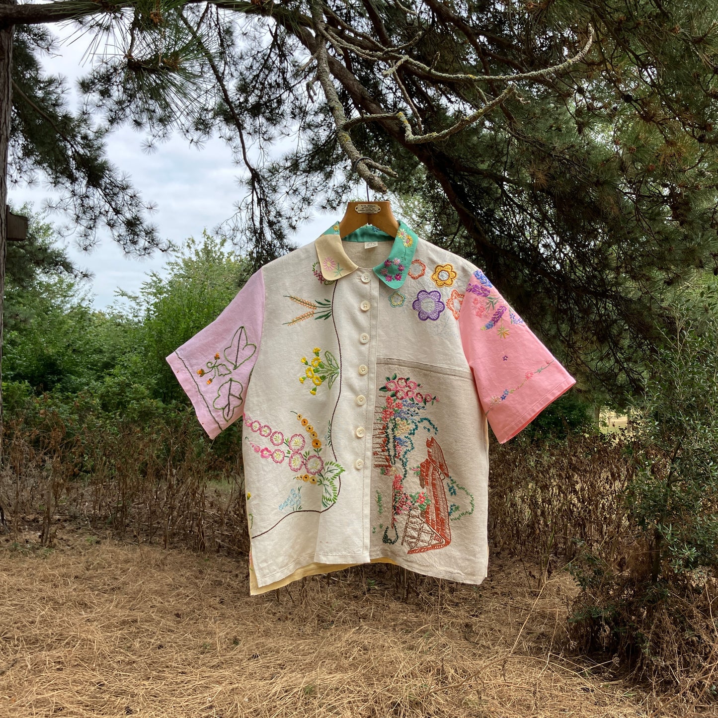 A short-sleeve button-front shirt made from reclaimed vintage tablecloths in neutrals with pink sleeves, and a light green collar.