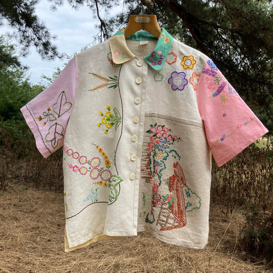 A short-sleeve button-front shirt made from reclaimed vintage tablecloths in neutrals with pink sleeves, and a light green collar.