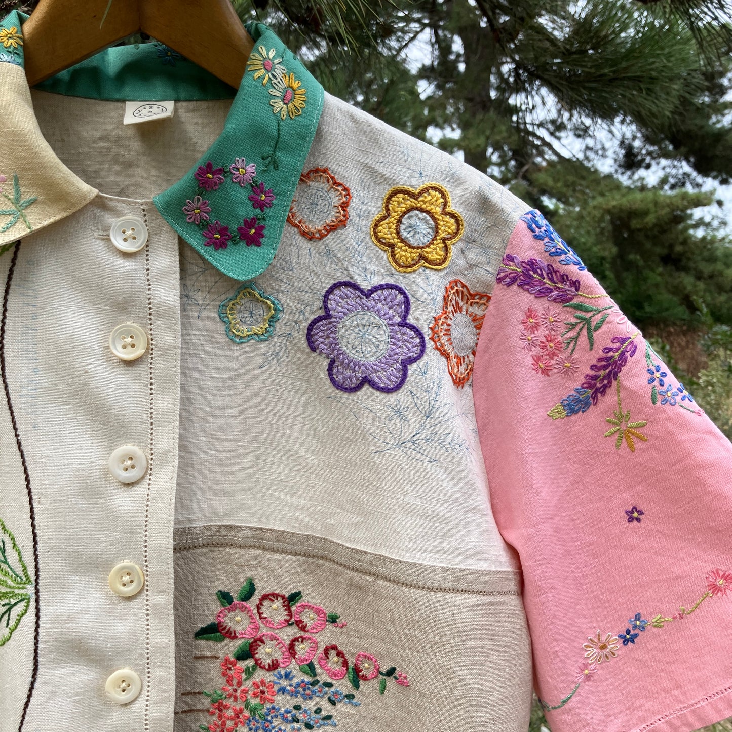 A short-sleeve button-front shirt made from reclaimed vintage tablecloths in neutrals with pink sleeves, and a light green collar.