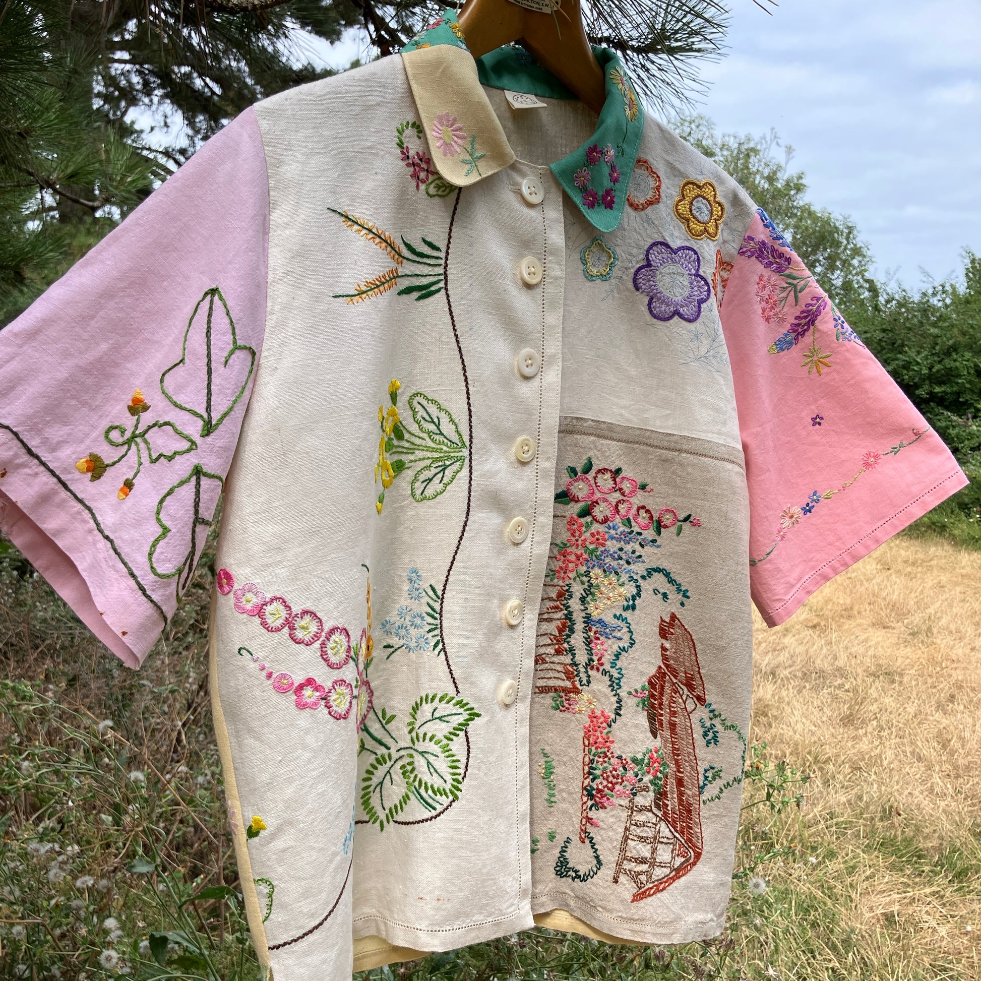 A short-sleeve button-front shirt made from reclaimed vintage tablecloths in neutrals with pink sleeves, and a light green collar.