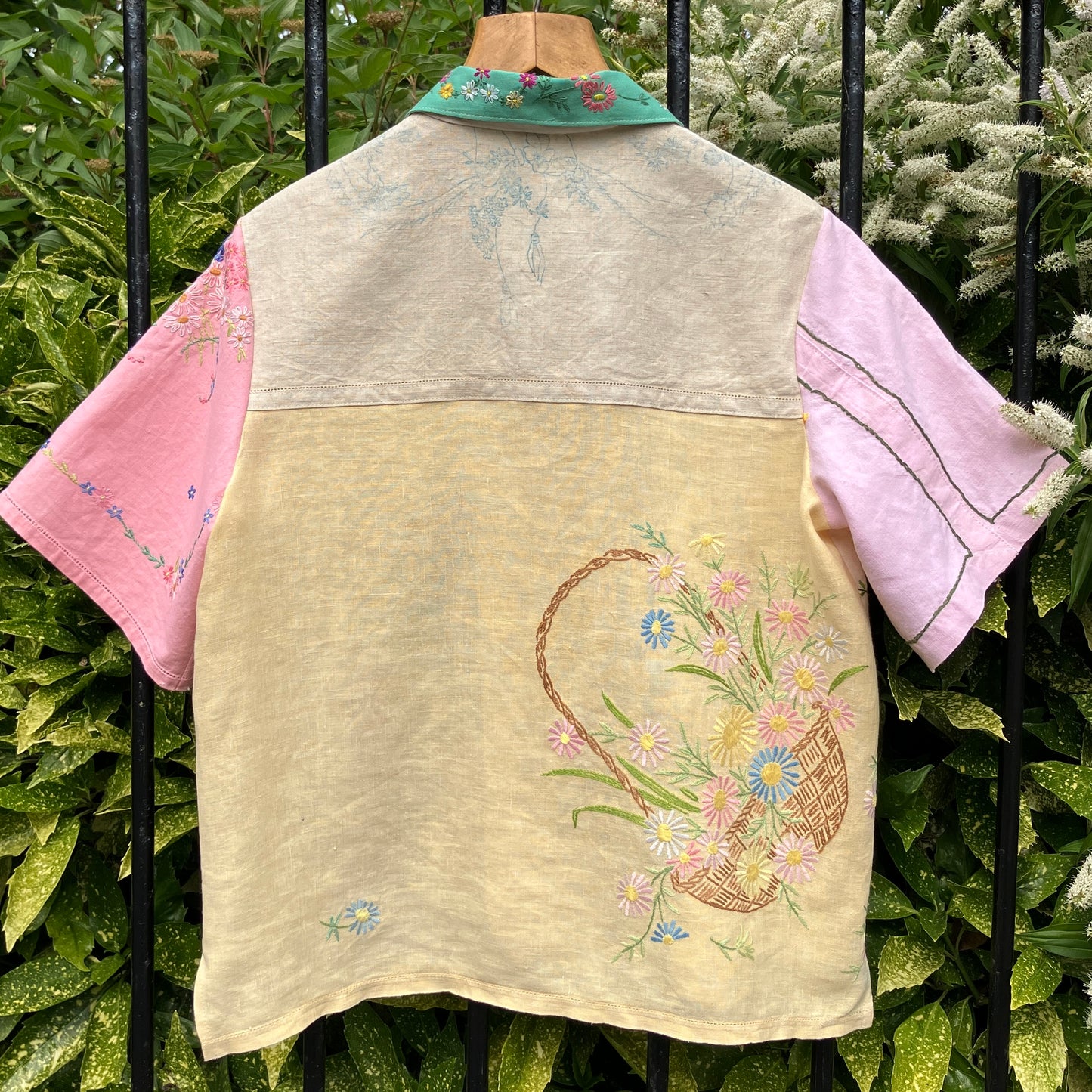 A short-sleeve button-front shirt made from reclaimed vintage tablecloths in neutrals with pink sleeves, and a light green collar.