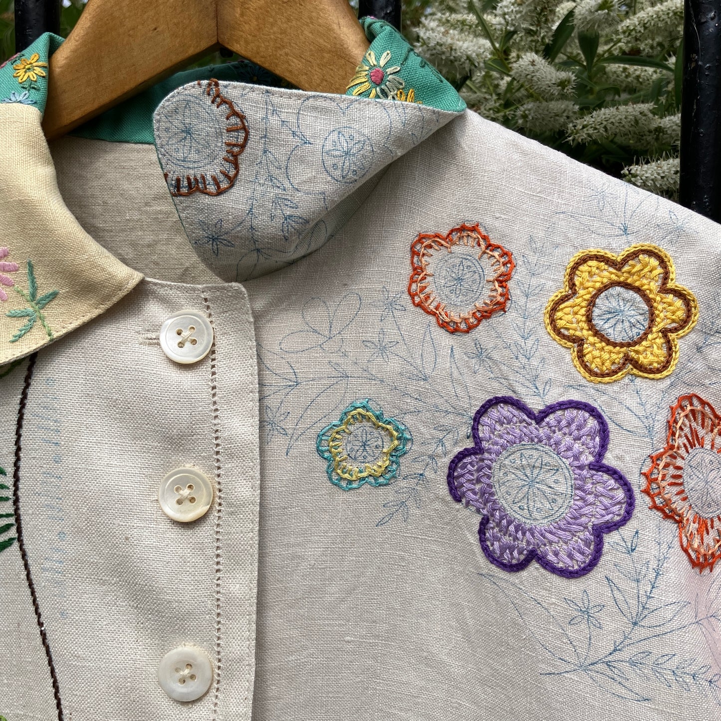 A short-sleeve button-front shirt made from reclaimed vintage tablecloths in neutrals with pink sleeves, and a light green collar.