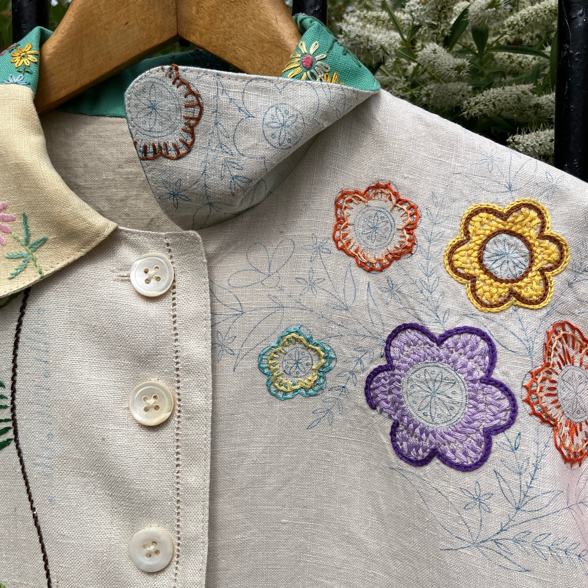 A short-sleeve button-front shirt made from reclaimed vintage tablecloths in neutrals with pink sleeves, and a light green collar.