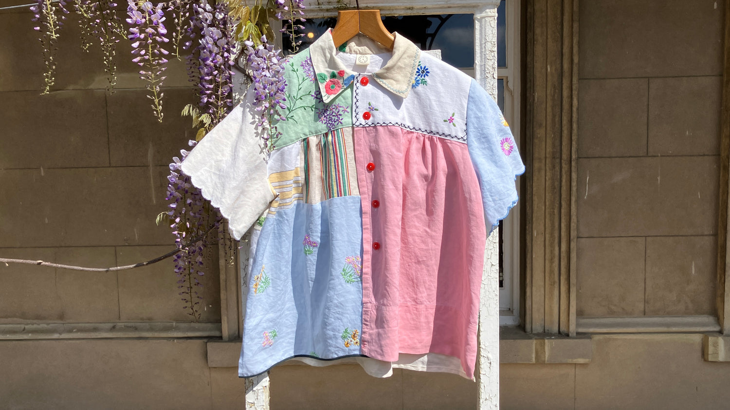 Summer shirt made from recycled vintage table linen in pastel colours with thrifted red buttons. Pictured with a hanging wisteria plant