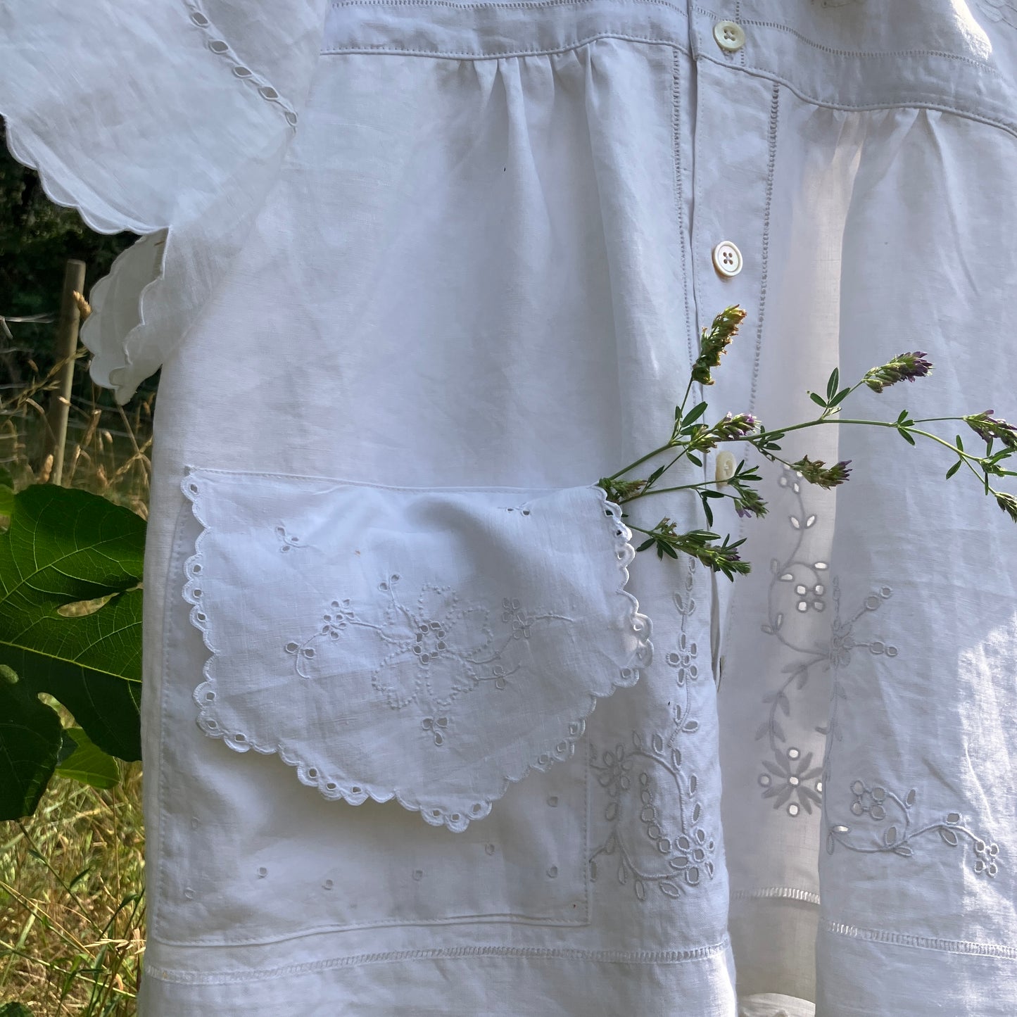 White embroidered blouse with a pocket detail against a natural background
