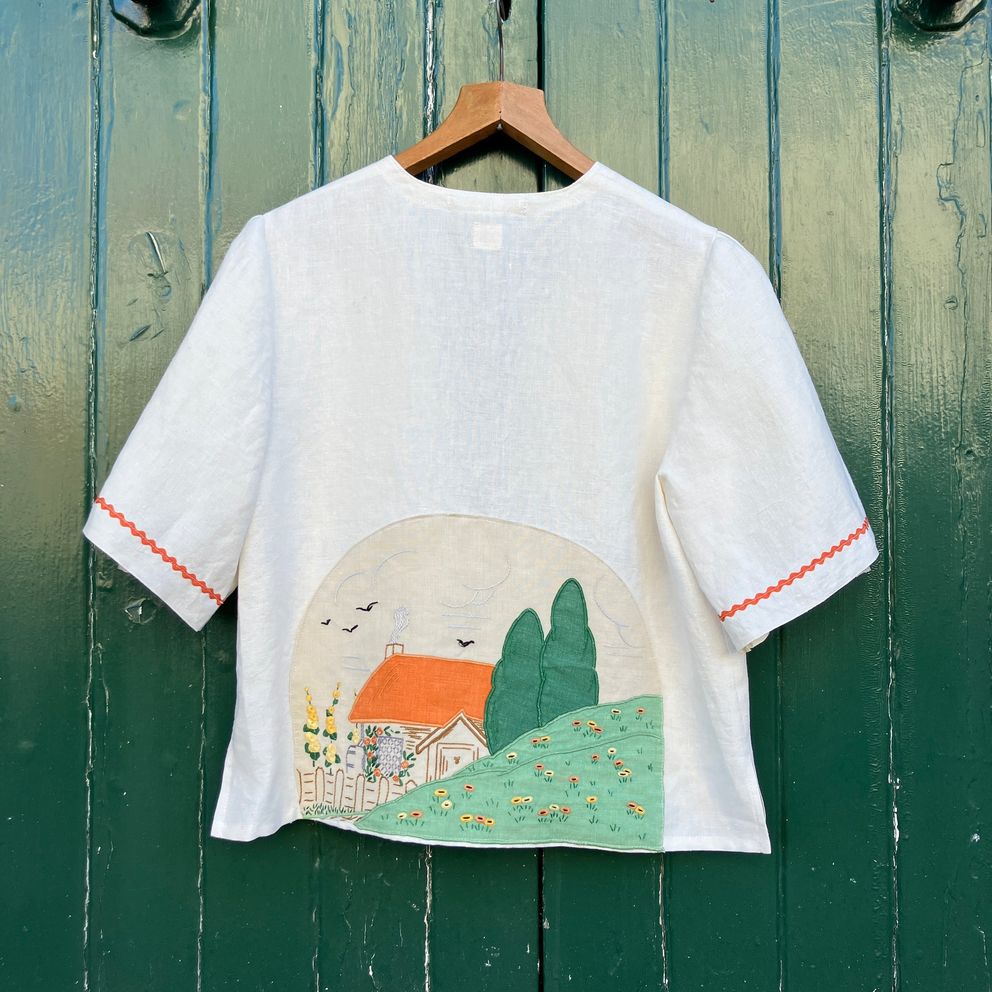 Simple linen shirt/jacket with patch pockets, ric-rac trim and a 1930s embroidered cottagecore scene appliquéd on to the back.