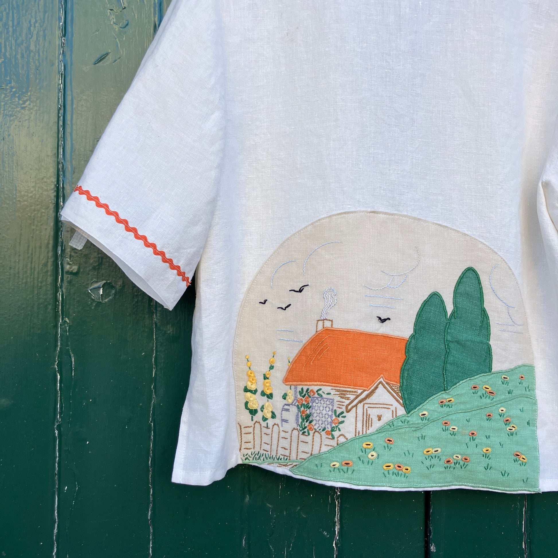 Simple linen shirt/jacket with patch pockets, ric-rac trim and a 1930s embroidered cottagecore scene appliquéd on to the back.