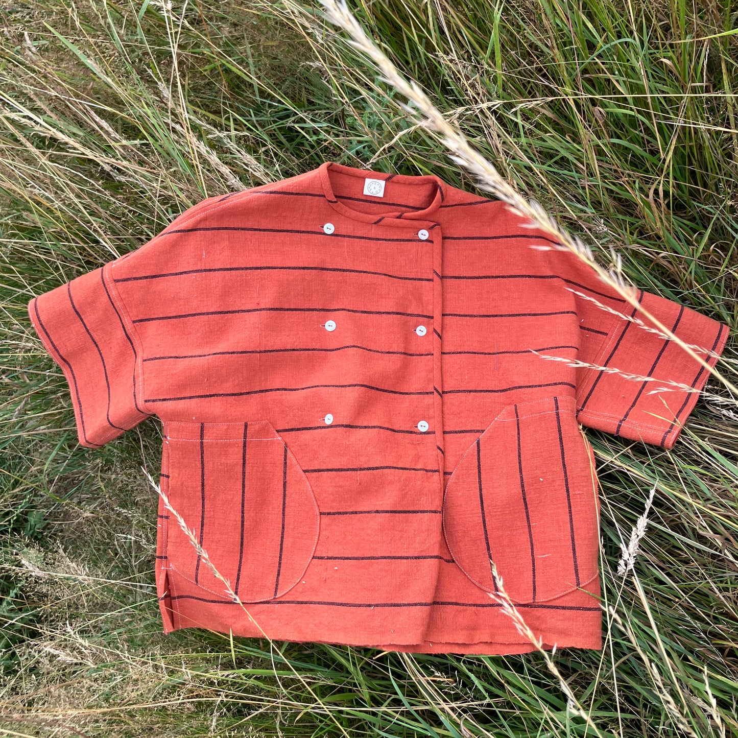 A terracotta orange boxy top with thin black stripes and a double-breasted front button closure