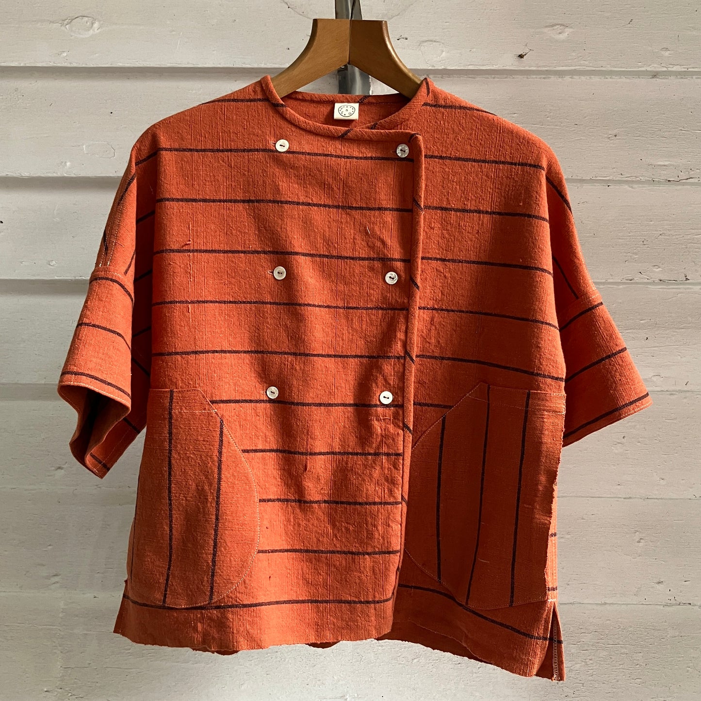 A terracotta orange boxy top with thin black stripes and a double-breasted front button closure