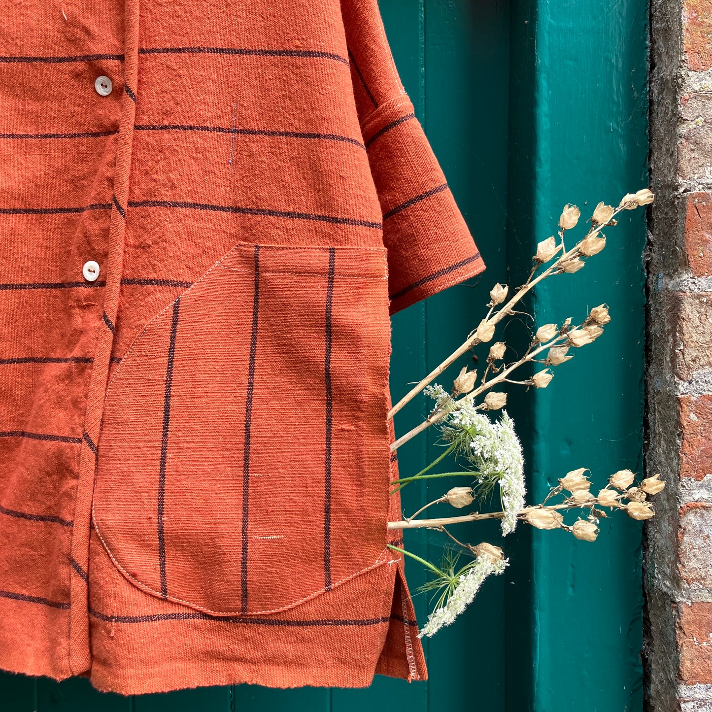 A terracotta orange boxy top with thin black stripes and a double-breasted front button closure