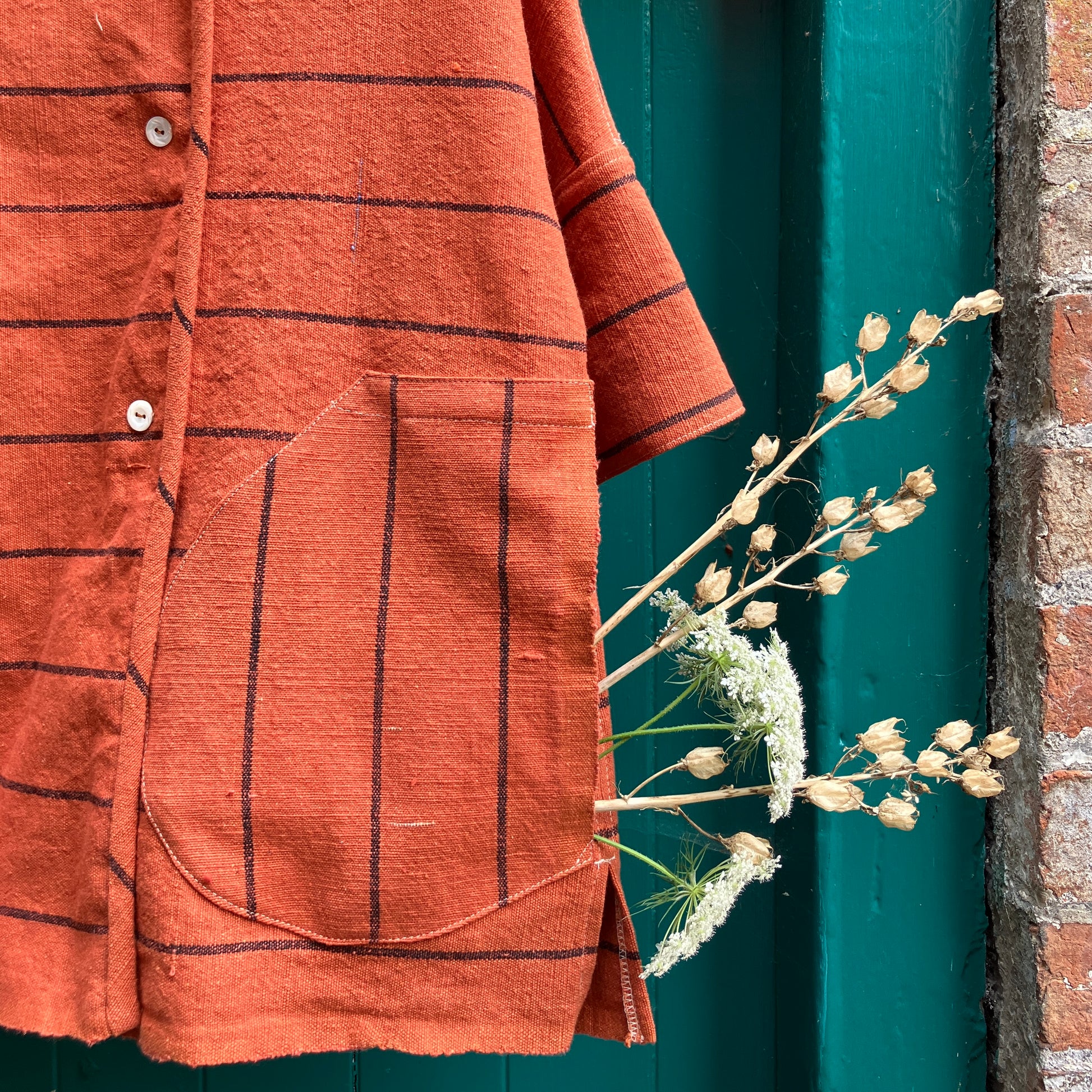 A terracotta orange boxy top with thin black stripes and a double-breasted front button closure