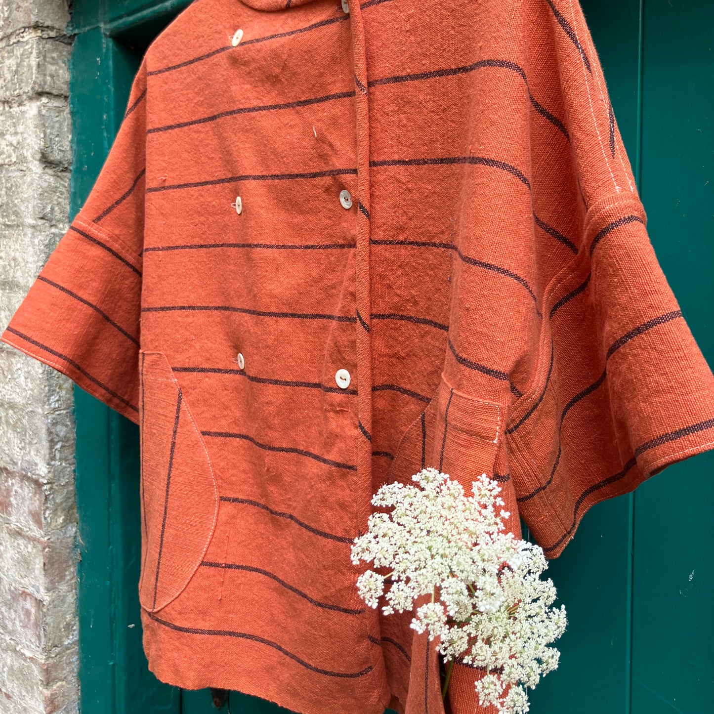 A terracotta orange boxy top with thin black stripes and a double-breasted front button closure