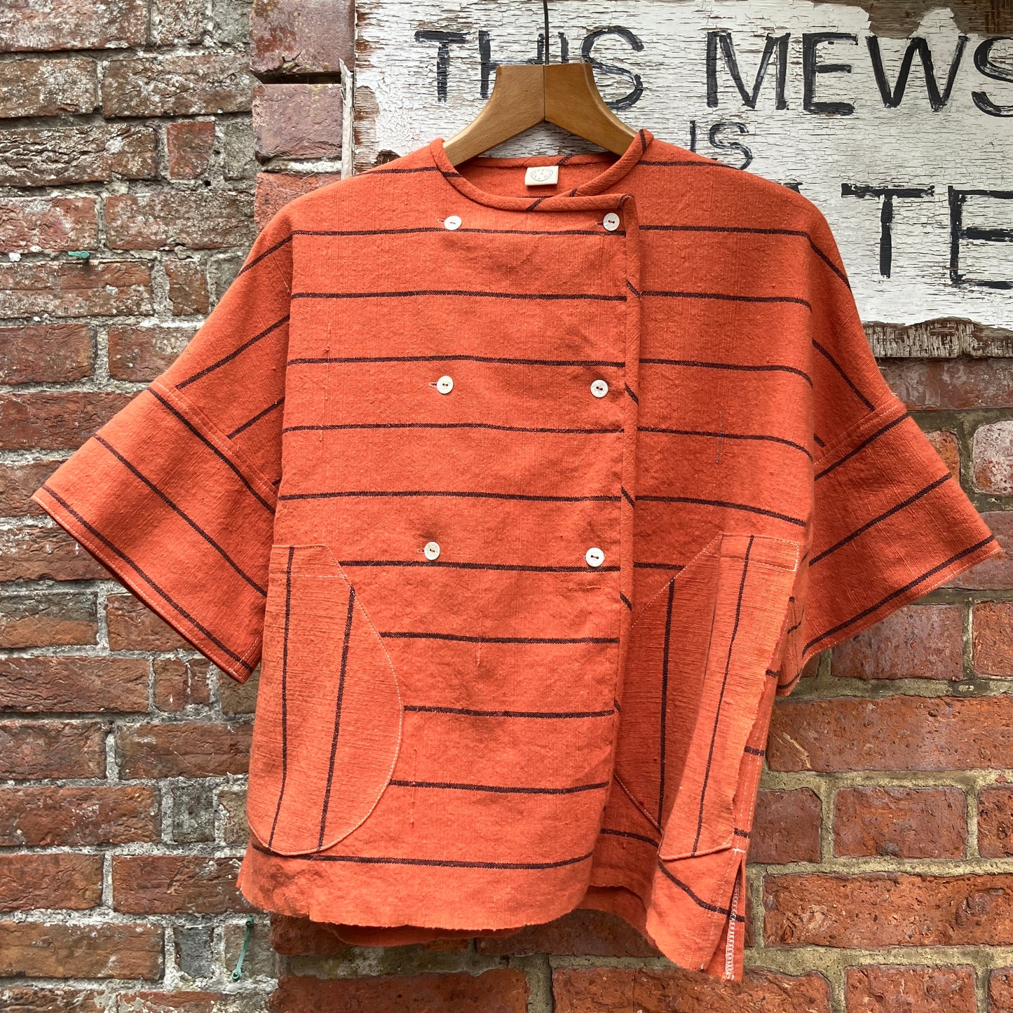 A terracotta orange boxy top with thin black stripes and a double-breasted front button closure