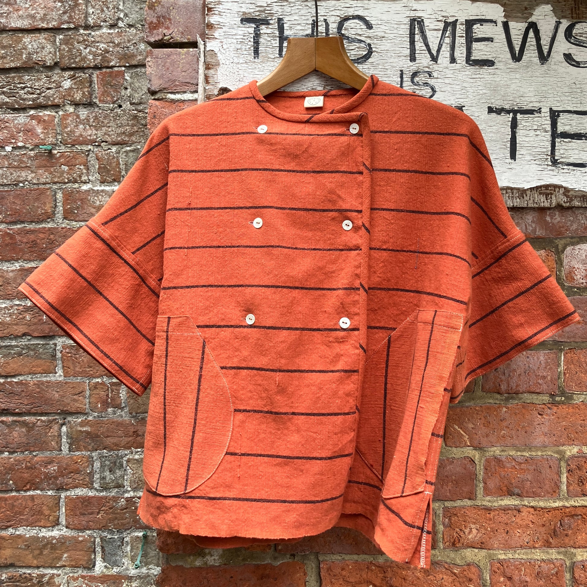 A terracotta orange boxy top with thin black stripes and a double-breasted front button closure