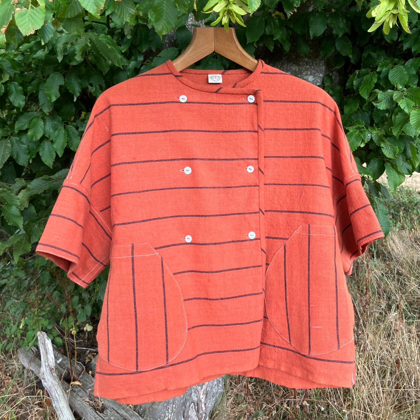 An orange short-sleeve linen shirt with thin black horizontal stripes, featuring  two large front patch pockets