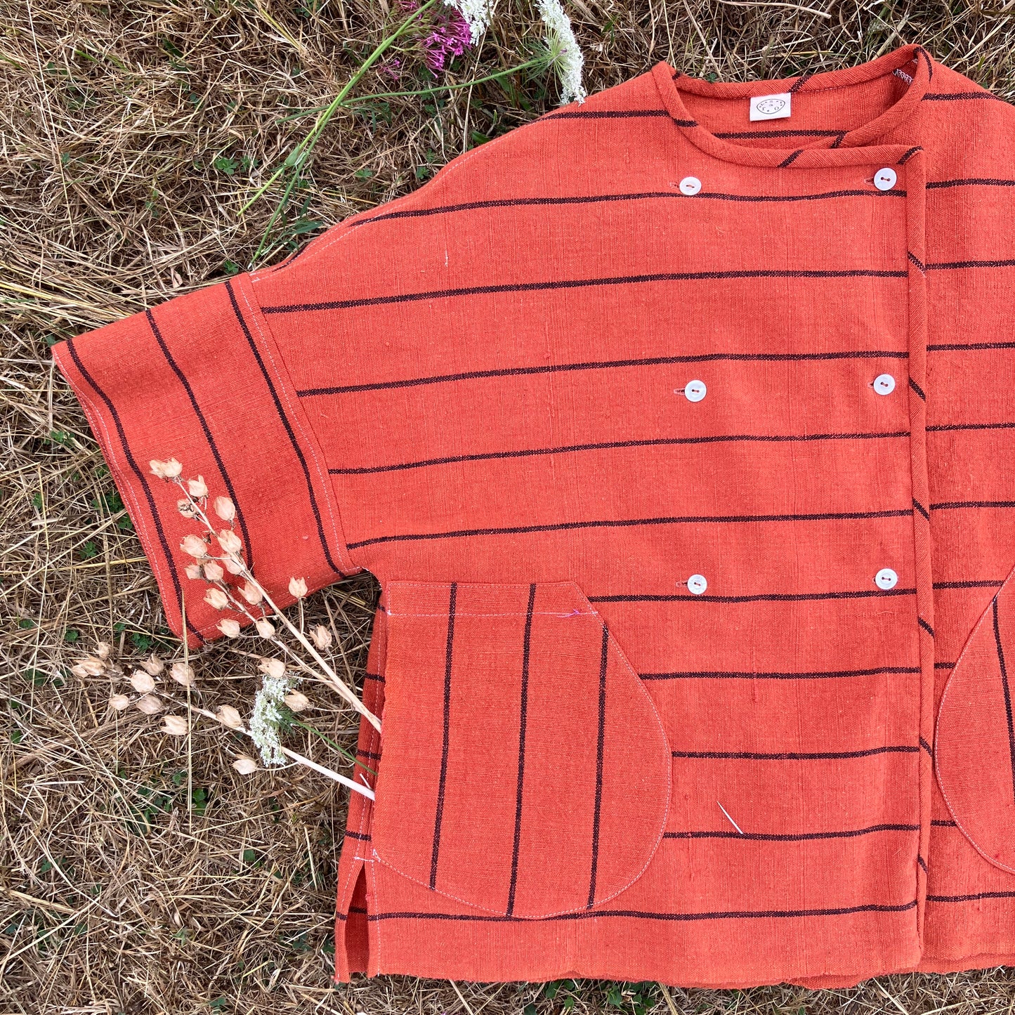 A terracotta orange boxy top with thin black stripes and a double-breasted front button closure