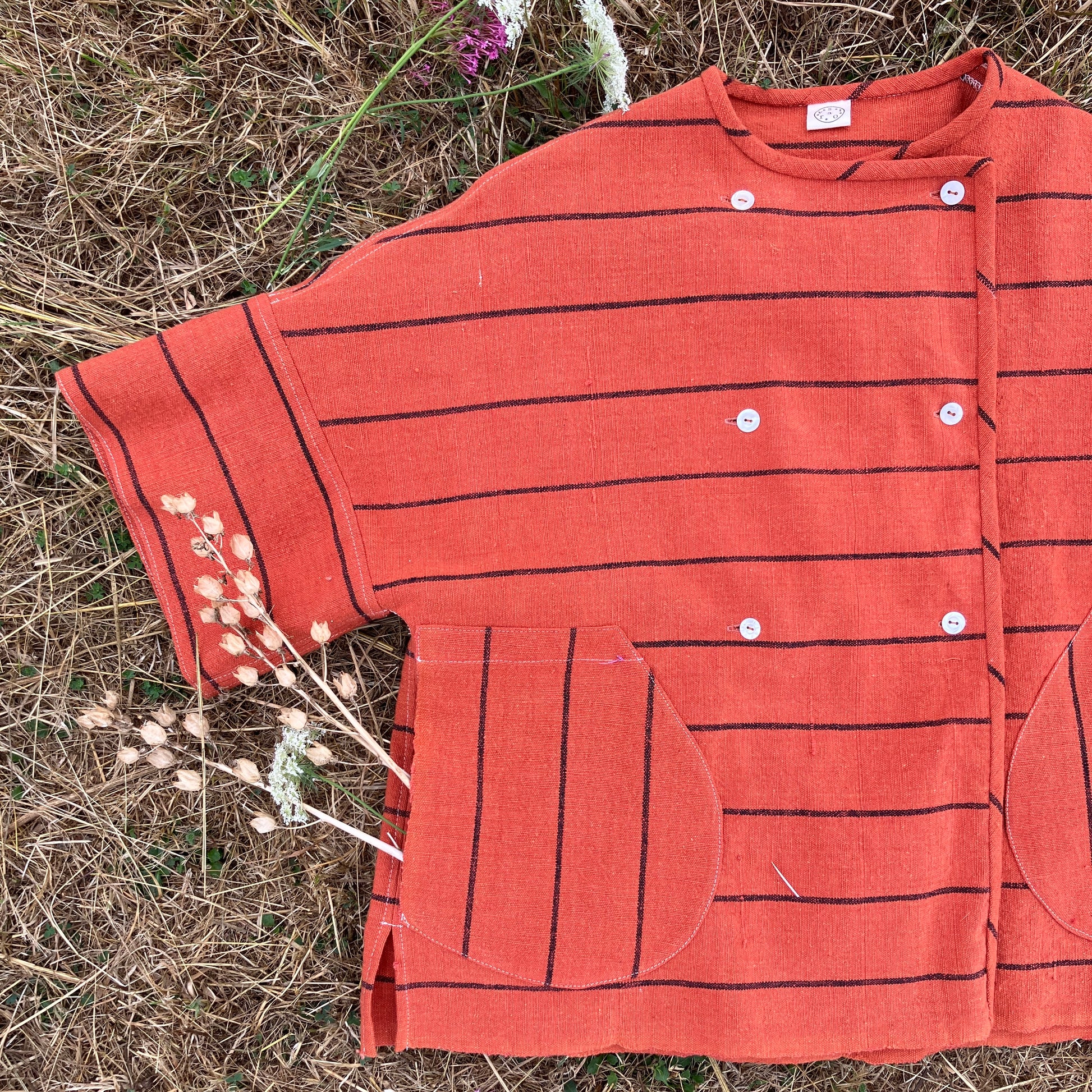 A terracotta orange boxy top with thin black stripes and a double-breasted front button closure
