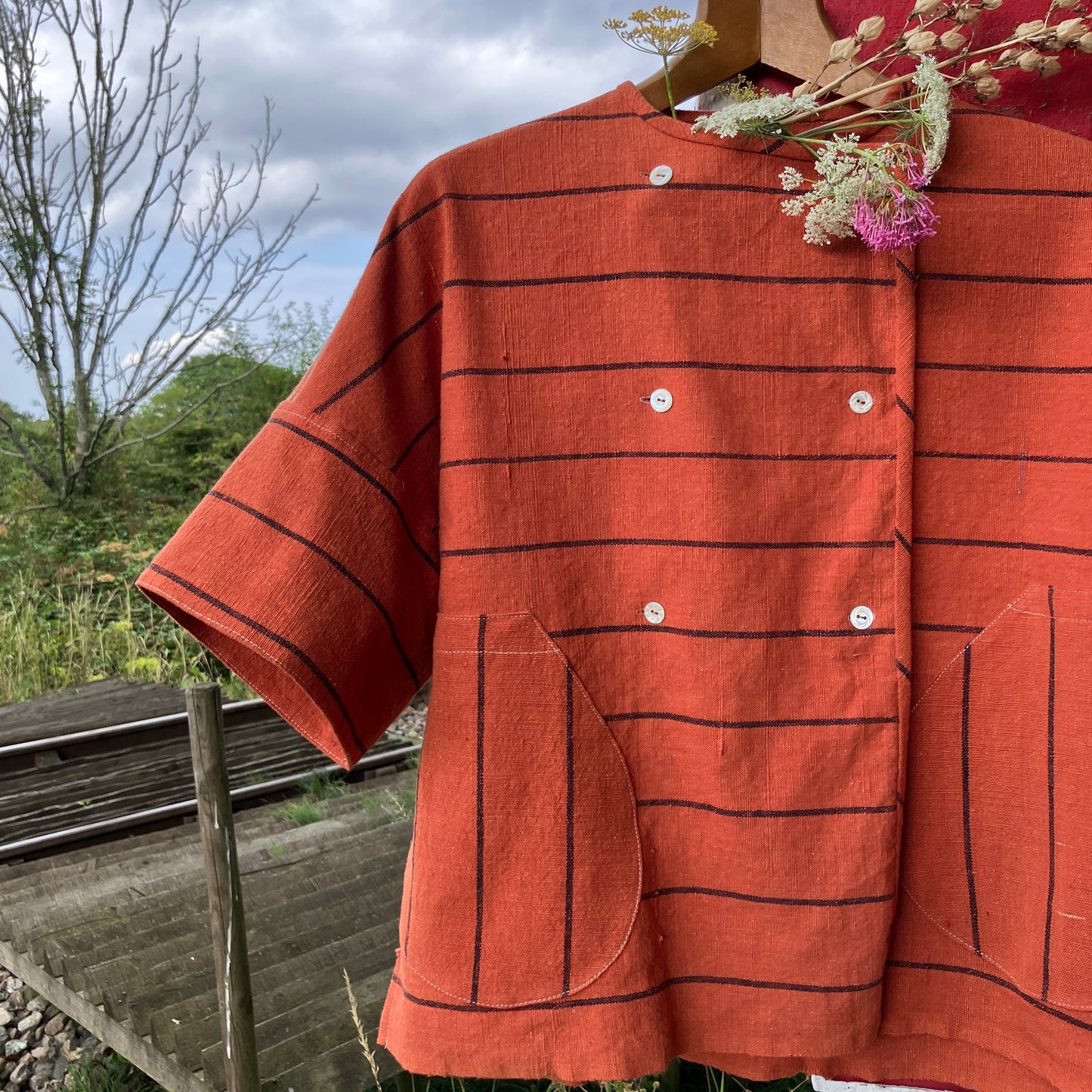 A terracotta orange boxy top with thin black stripes and a double-breasted front button closure