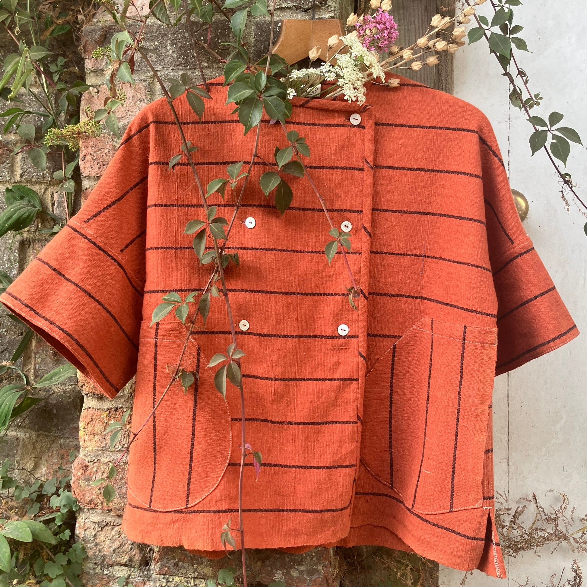 A terracotta orange boxy top with thin black stripes and a double-breasted front button closure