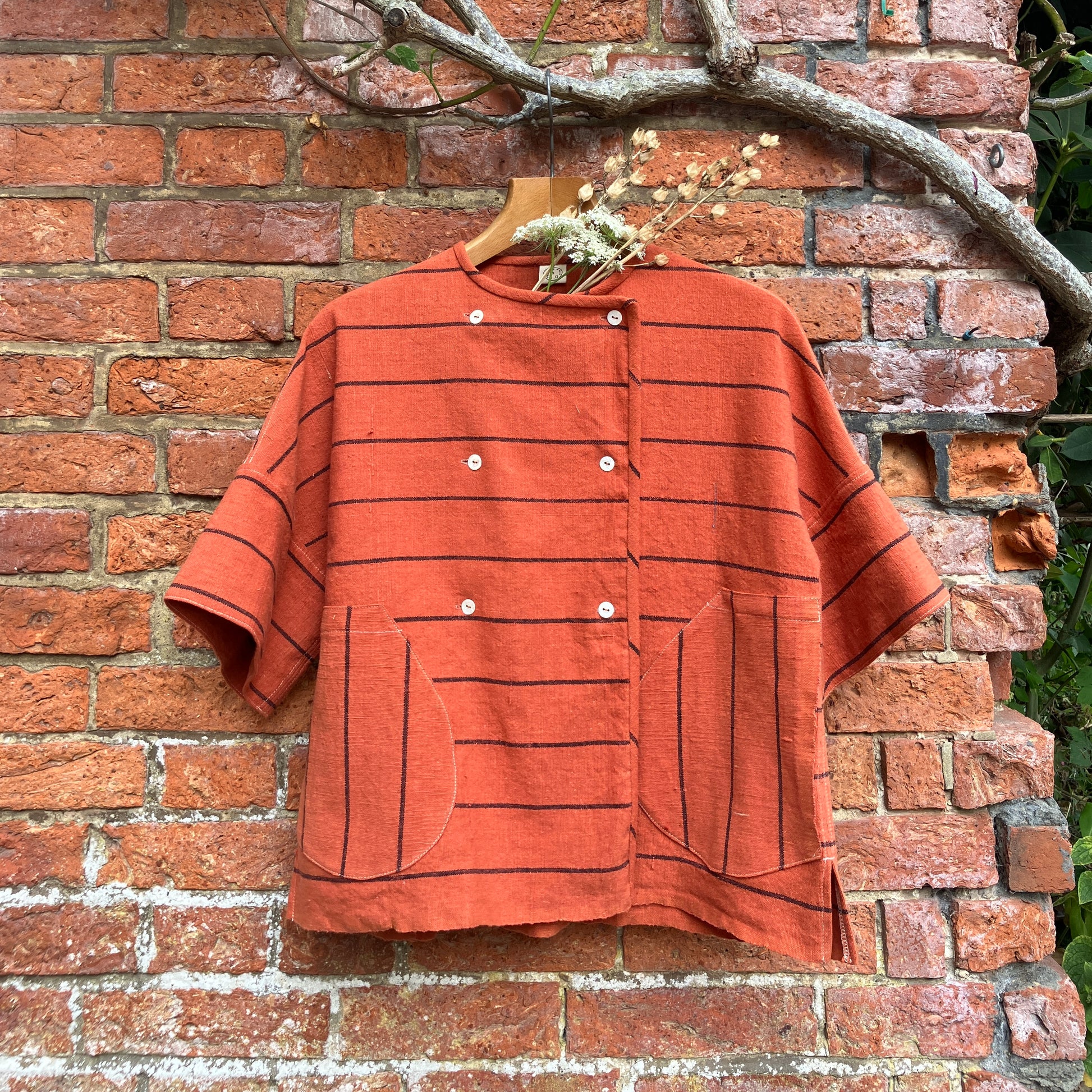 A terracotta orange boxy top with thin black stripes and a double-breasted front button closure