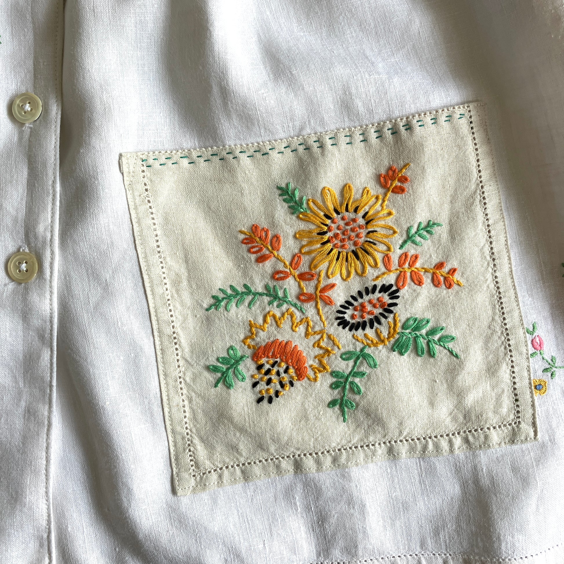 Short sleeved shirt made from a patchwork of reclaimed tablecloths with a traditional English pub with a thatched roof embroidered on the front and two bows on the yoke (detail of pocket)