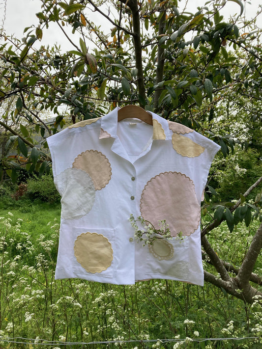 Handmade boxy shirt decorated with appliqué scallop-edge doilies shown hanging in a tree