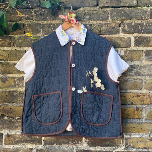 Super useful vest/gilet/bodywarmer/waistcoat handmade from a reclaimed black cotton quilt. Features two large patch pockets, three found shell buttons and brown linen binding. 