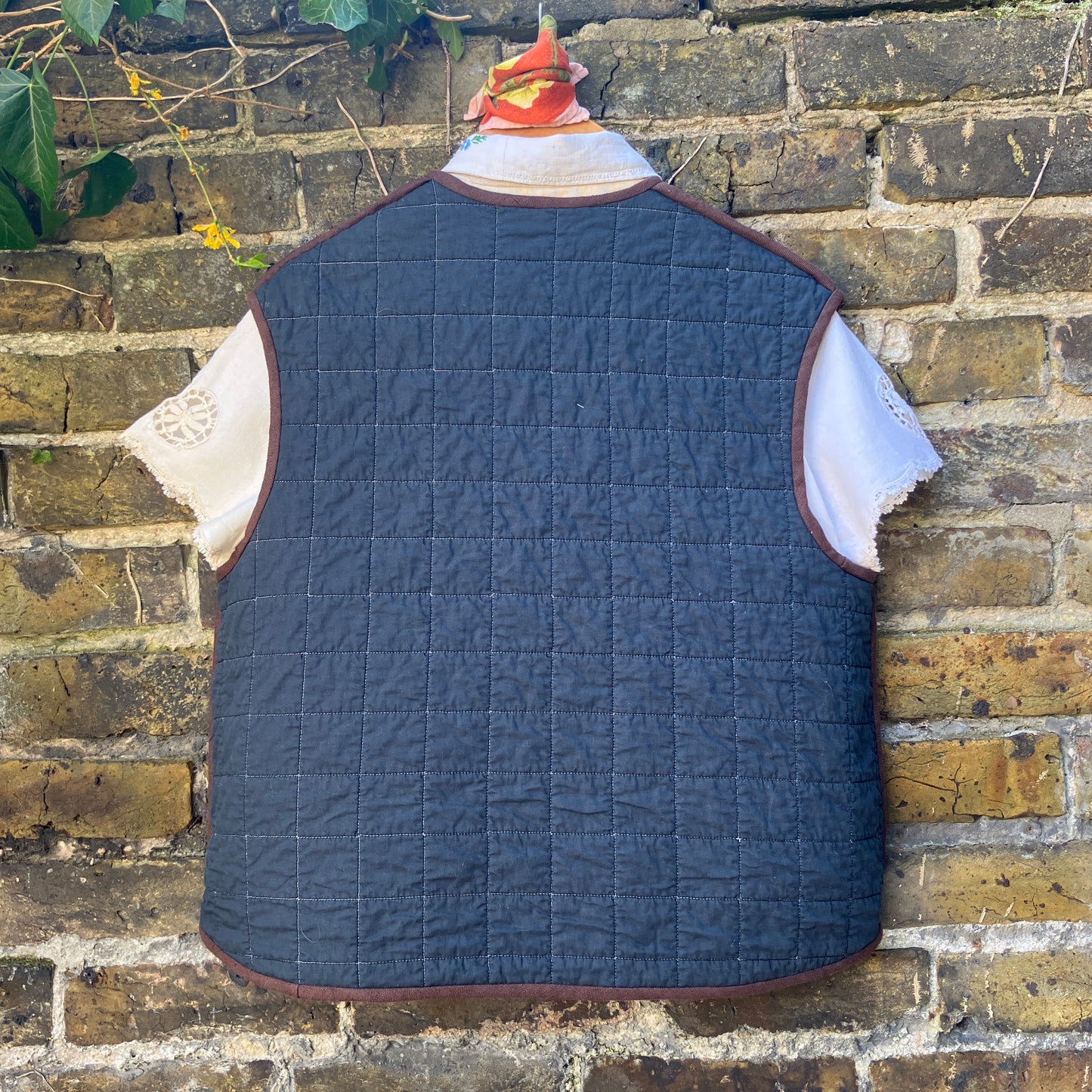 Super useful vest/gilet/bodywarmer/waistcoat handmade from a reclaimed black cotton quilt. Features two large patch pockets, three found shell buttons and brown linen binding (back view)
