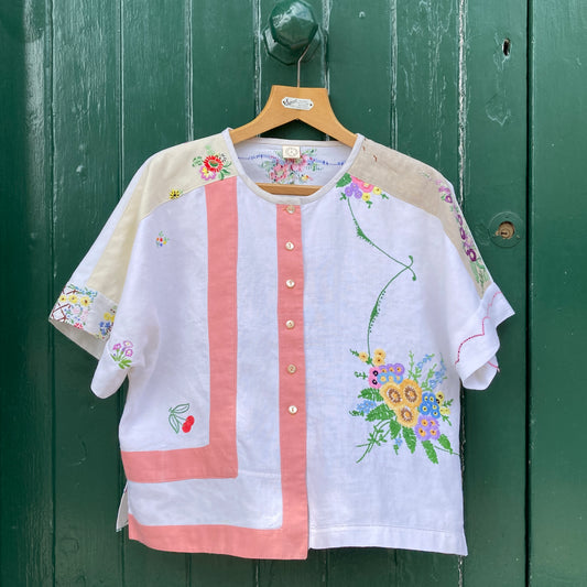 Short-sleeved boxy top made from vintage embroidered linen tablecloths. Mostly white and off-white with wide pink stripes and embroidered details include cherries and flowers.