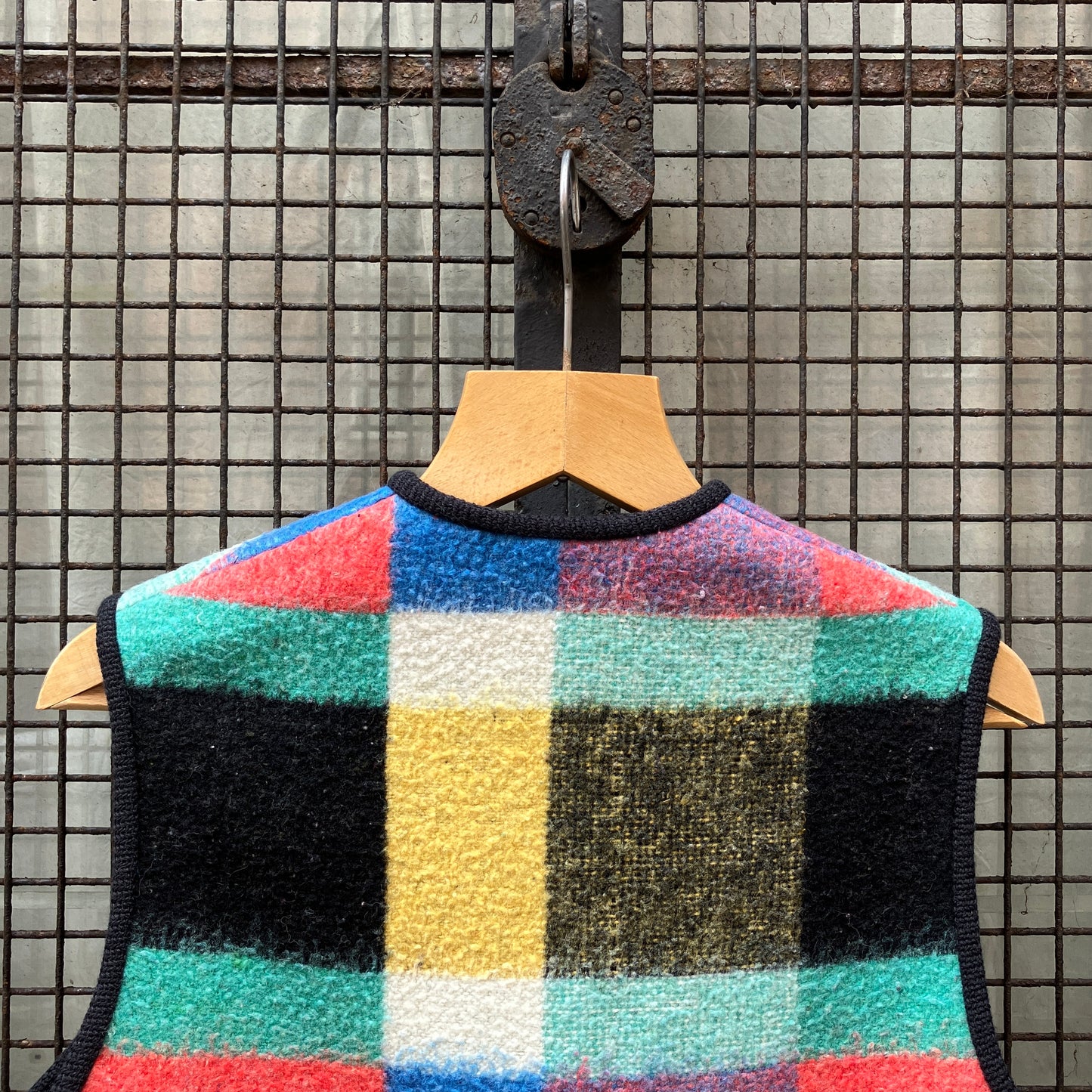 A vest/gilet/waistcoat made from a multicoloured checked reclaimed blanket. It fastens with three wooden buttons and has to large patch pockets (close-up of back)
