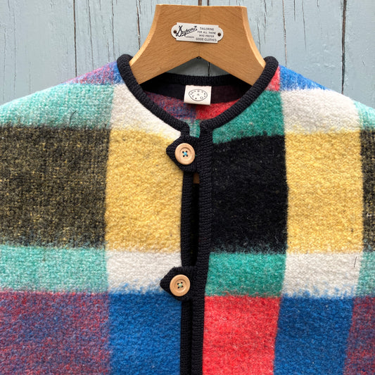 Close-up of a vest/gilet/waistcoat made from a multicolour checked reclaimed blanket. It fastens with three wooden buttons and has to large patch pockets