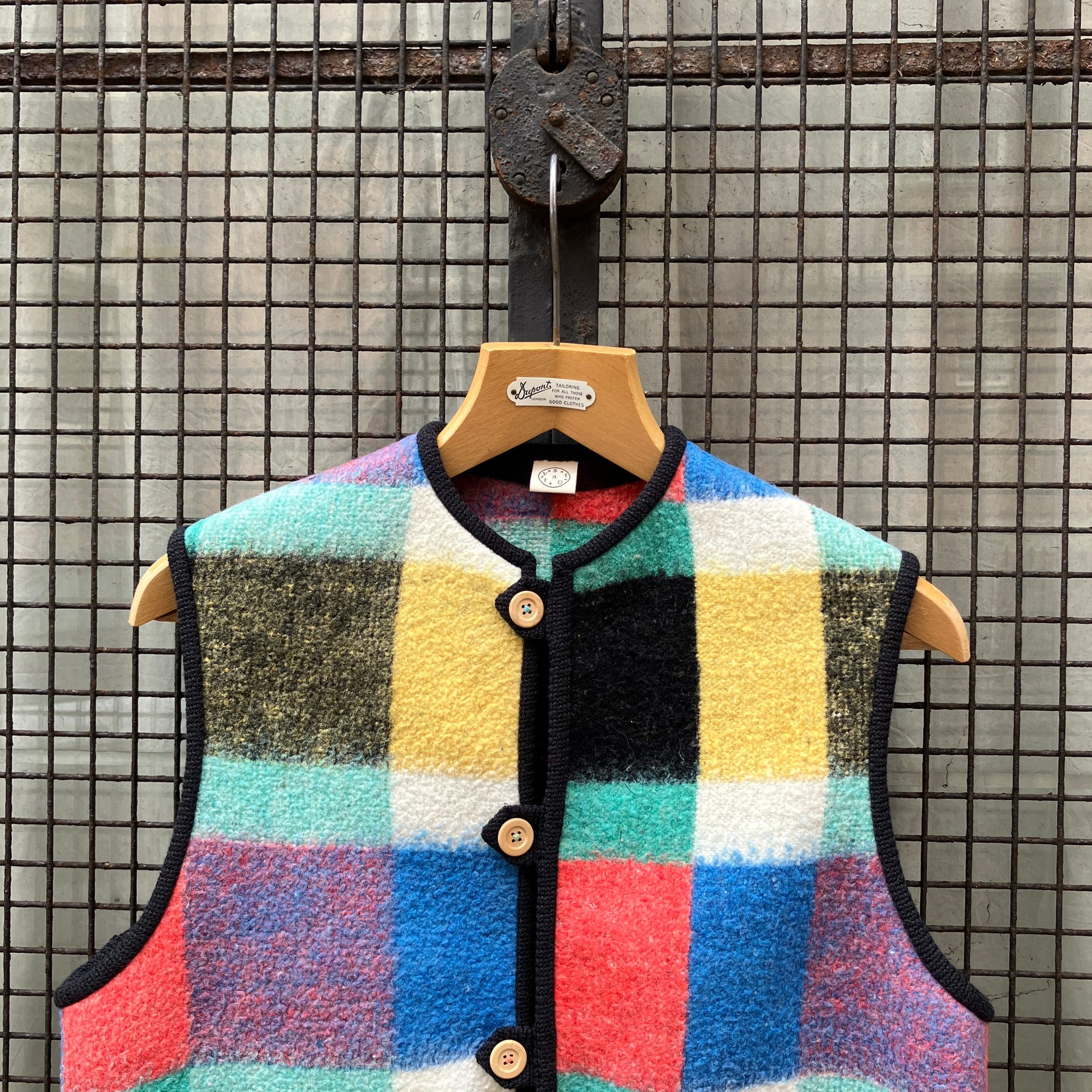 A vest/gilet/waistcoat made from a multicoloured checked reclaimed blanket. It fastens with three wooden buttons and has to large patch pockets