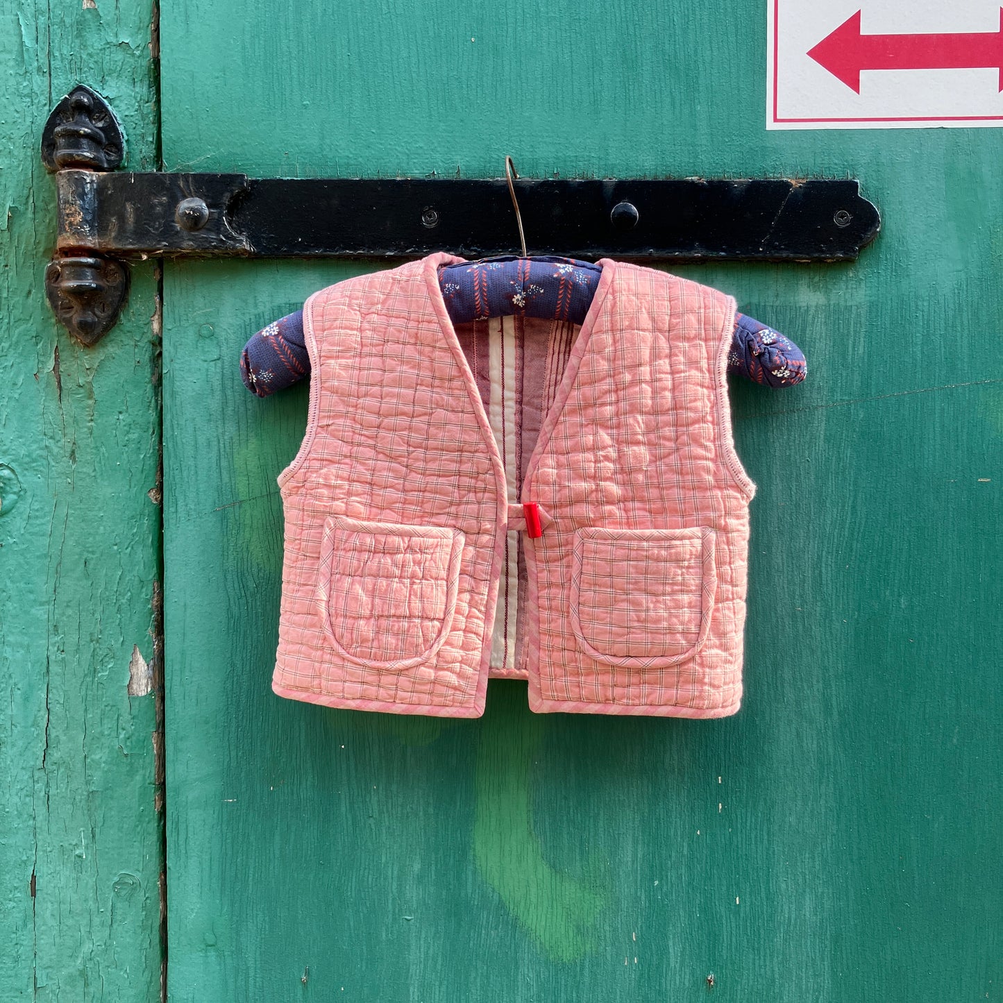 kids vest/gilet/waistcoat made from offcuts of a reclaimed pink quilt. Shown hanging on a blue vintage hanger against a green gate
