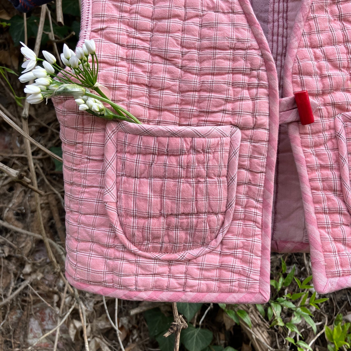 kids vest/gilet/waistcoat made from offcuts of a reclaimed pink quilt. Close-up of some wild flowers in one of the pockets