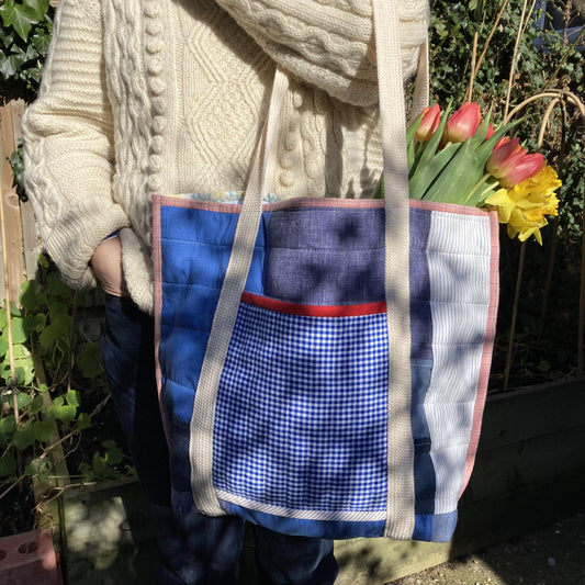 A woman in an arran sweater holds a quilted patchwork tote bag hand made from reclaimed cotton shirts, with a bunch of red tulips sticking out the top