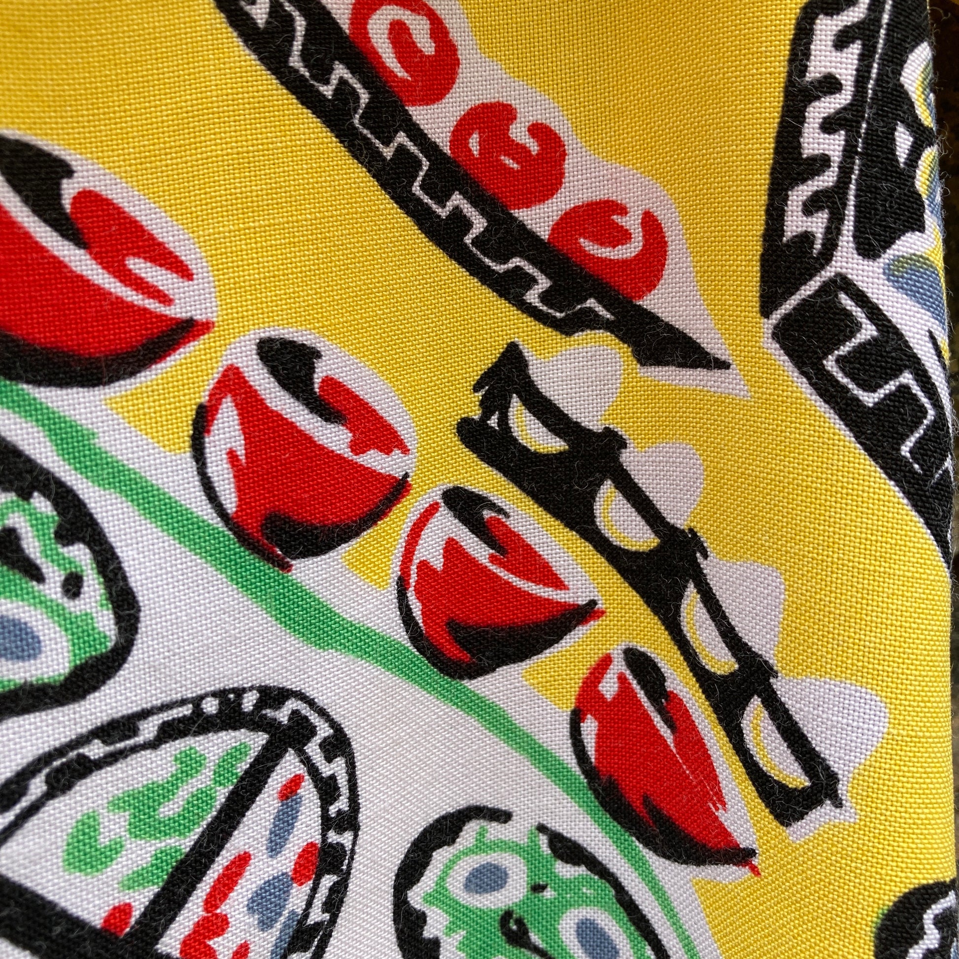 short-sleeved shirt made from a recycled tablecloth printed with picnic food a record player and records, mainly yellow and white, hanging on a hanger against a brick wall (close up of eggs print)