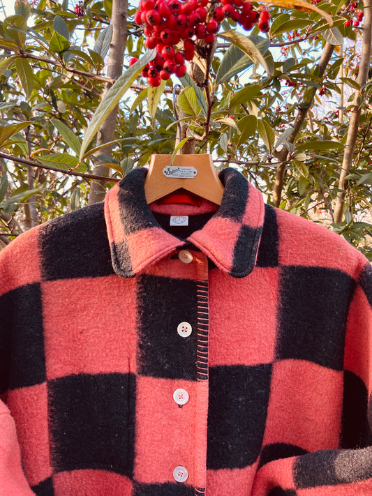 Pink and black checkerboard blanket jacket handmade from a reclaimed blanket. Pictured hanging in a tree with red berries